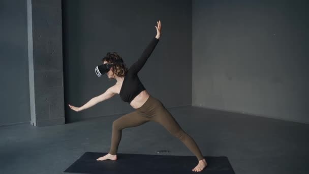Νεαρή γυναίκα ασκεί ασκήσεις γιόγκα στο στούντιο χρησιμοποιώντας γυαλιά εικονικής πραγματικότητας - Πλάνα, βίντεο