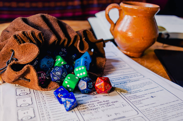 Roleplaying dice of various shapes and colors spilling out of a leather dice bag on a character sheet. With in the background an open notebook and and mobile phone - Photo, Image