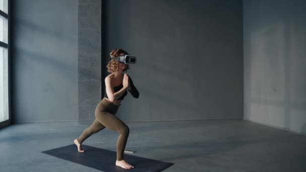 Jeune femme pratiquant des exercices de yoga en studio en utilisant un casque de réalité virtuelle - Séquence, vidéo
