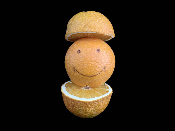 Orange mûr avec un motif sourire. Fruits jaunes, entiers et coupés, isolés sur du noir. Agrumes avec une photo d'un visage joyeux. Concept : joie, positif, sourire, bonheur - Photo, image