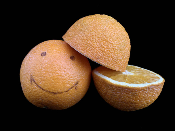 Naranja maduro con un patrón de sonrisa. Frutos amarillos, enteros y en un corte, aislados sobre negro. Cítricos con una imagen de una cara alegre. Concepto: alegría, positivo, sonrisa, felicidad - Foto, Imagen