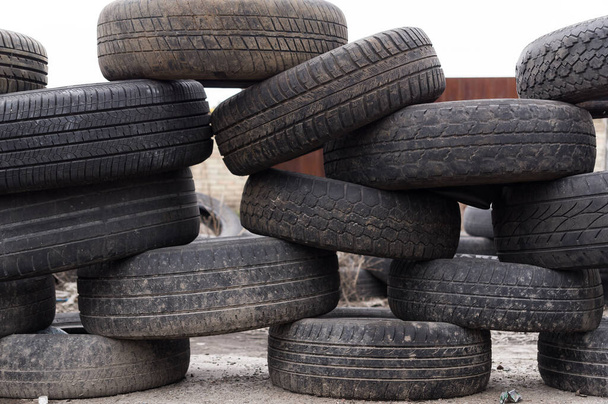 Una pared de ruedas estropeadas. Esgrima hecha de neumáticos viejos para ruedas de coche. Volcado de ruedas. Luz del día. - Foto, imagen