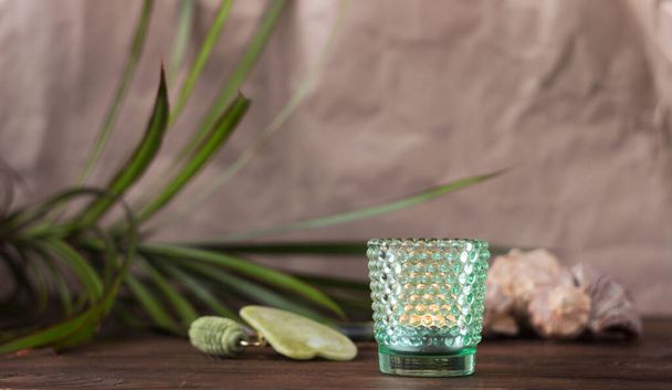 Set de massage : gouache verte et rouleau de jade. Fond en bois, feuilles de plantes, bougie dans un verre à picots - Photo, image