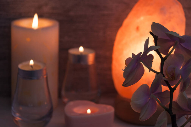 Λαμπτήρας αλατιού Ιμαλαΐων με ορχιδέα λουλούδι, κεριά, θολή στο σκοτεινό δωμάτιο. Spa, χαλαρώστε έννοια. - Φωτογραφία, εικόνα