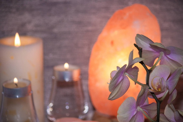 Гималайская соляная лампа с цветком орхидеи, свечи в темной комнате. Спа, концепция отдыха. - Фото, изображение