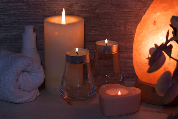 Гималайская соляная лампа с цветком орхидеи, маслом, полотенцем, свечами в темной комнате. Спа, концепция отдыха. - Фото, изображение