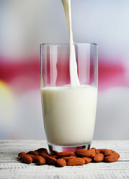 Almond milk is poured into glass, on color wooden table, on light background - Foto, Bild
