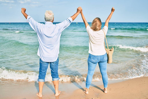 Испанская пара средних лет дышит с поднятыми на пляже руками. - Фото, изображение