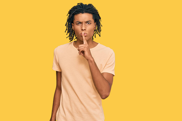 若いアフリカ系アメリカ人の男性は、唇に指で静かになるように頼むカジュアルな服を着ていた。沈黙と秘密の概念.  - 写真・画像
