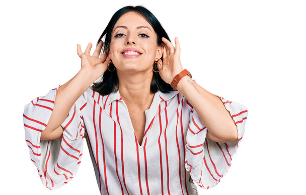 Joven chica hispana vestida con ropa casual tratando de escuchar el gesto de las dos manos en la oreja, curiosa de chismes. problema auditivo, sordo  - Foto, Imagen