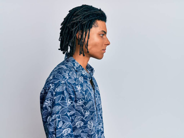 Jeune homme afro-américain portant une chemise de style années 80 regardant vers le côté, pose de profil relax avec un visage naturel avec un sourire confiant.  - Photo, image