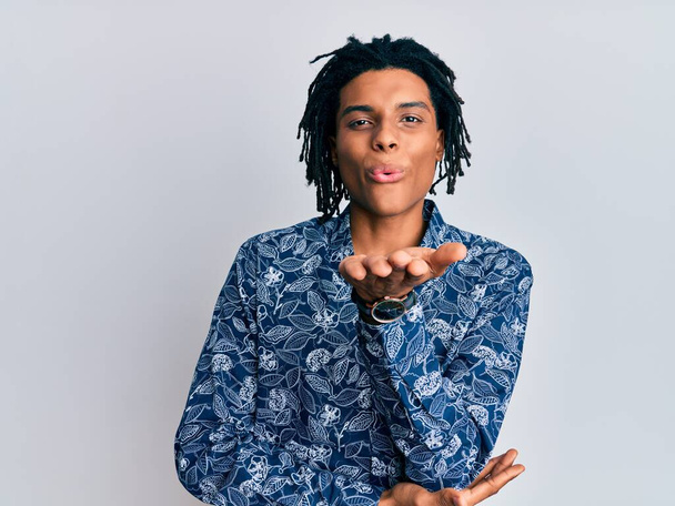 Jovem afro-americano vestindo camisa de estilo dos anos 80 olhando para a câmera soprando um beijo com a mão no ar sendo adorável e sexy. expressão do amor.  - Foto, Imagem