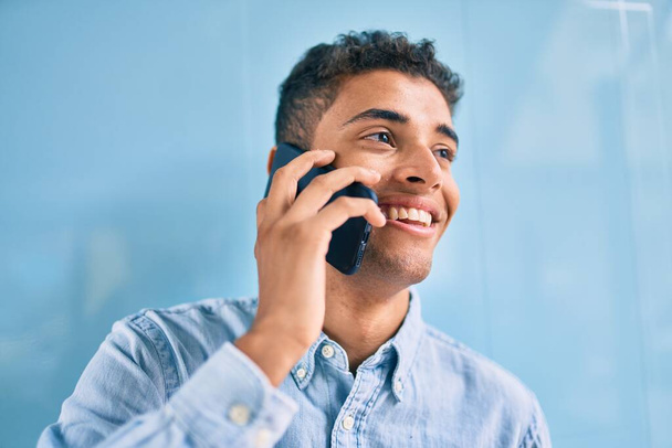 Молодий латинський чоловік посміхається щасливим розмовляти по смартфону в місті
. - Фото, зображення
