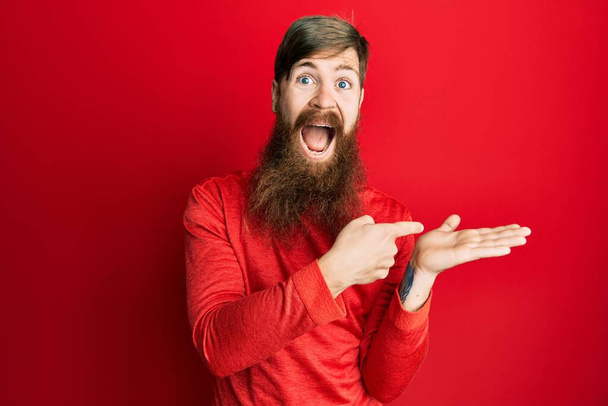 Redhead man with long beard pointing open palm with finger celebrating crazy and amazed for success with open eyes screaming excited.  - Zdjęcie, obraz