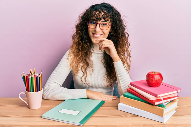 Young hispanic girl studying for school exam smiling looking confident at the camera with crossed arms and hand on chin. thinking positive.  - Photo, Image