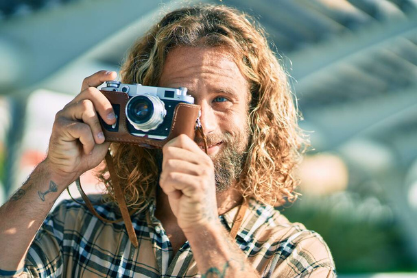 Nuori valkoihoinen turisti mies hymyilee onnellinen käyttäen vintage kamera puistossa. - Valokuva, kuva