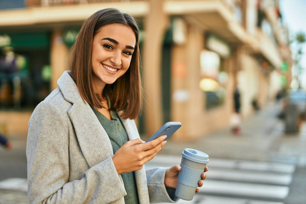 Молода іспаномовна дівчина використовує смартфон п'є каву в місті
. - Фото, зображення