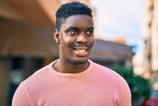 Νεαρός Αφροαμερικάνος χαμογελάει χαρούμενος που στέκεται στην πόλη. - Φωτογραφία, εικόνα