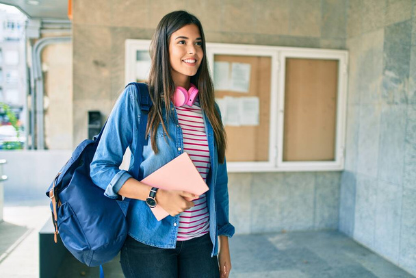 Νεαρή Ισπανίδα φοιτήτρια χαμογελά ευτυχισμένη με ακουστικά στο πανεπιστήμιο. - Φωτογραφία, εικόνα