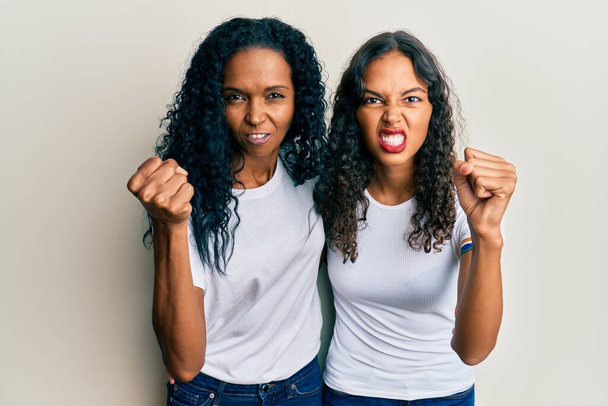 Afroamerykanka matka i córka noszą luźne białe koszulki zirytowane i sfrustrowane krzyki z gniewu, krzycząc szalony z gniewu i podniesione ręce  - Zdjęcie, obraz