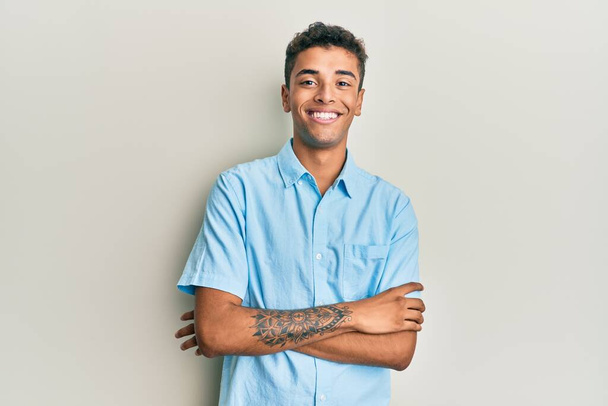 Joven hombre afroamericano guapo vistiendo ropa casual cara feliz sonriendo con los brazos cruzados mirando a la cámara. persona positiva.  - Foto, imagen