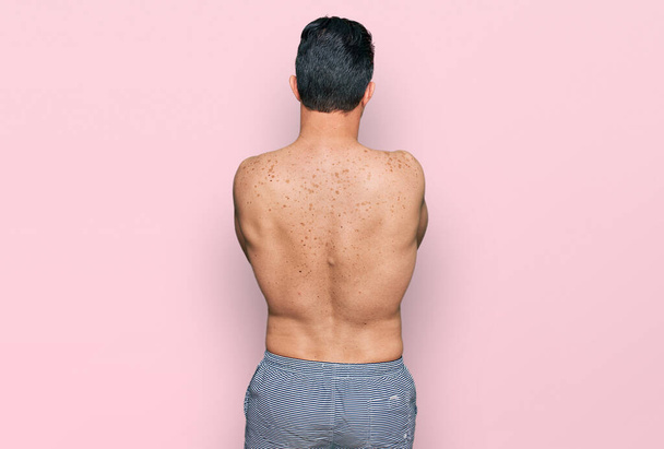 Beau jeune homme portant des maillots de bain torse nu debout vers l'arrière regardant loin avec les bras croisés  - Photo, image