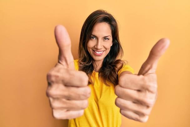 Young latin woman wearing casual clothes approving doing positive gesture with hand, thumbs up smiling and happy for success. winner gesture.  - Photo, Image