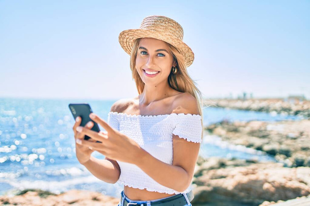 Молодая блондинка-туристка улыбается счастливой, используя смартфон на набережной. - Фото, изображение