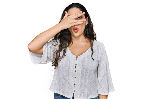 Brunette young woman wearing casual clothes peeking in shock covering face and eyes with hand, looking through fingers with embarrassed expression.  - Photo, Image