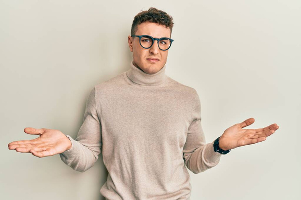 Hispanic young man wearing casual turtleneck sweater clueless and confused with open arms, no idea concept.  - Photo, image
