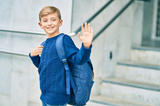 Adorable blond student kid saying goodbye with hand getting in the school. - 写真・画像