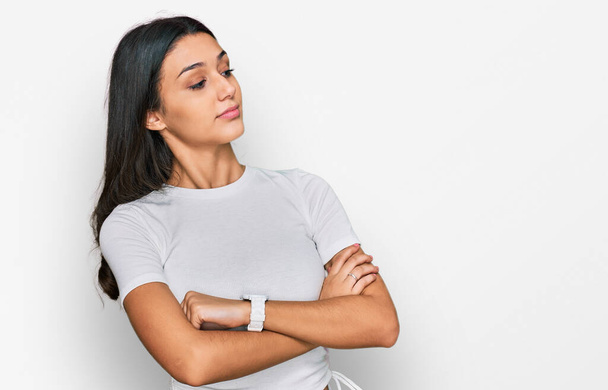 Young hispanic girl wearing casual white t shirt looking to the side with arms crossed convinced and confident  - Photo, Image