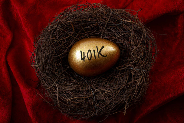 Индивидуальный пенсионный счет, концепция личных сбережений и пенсионного фонда с крупным планом золотого яйца в гнезде, символизирующим накопленное богатство с текстом 401k, изолированным на красном бархатном фоне - Фото, изображение