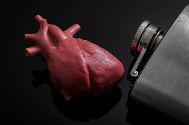 Αλκοολική καρδιακή ανεπάρκεια και βλάβη ή καρδιομυοπάθεια έννοια με μια καρδιά δίπλα σε μια μεταλλική φιάλη αλκοόλ. Καρδιομυοπάθεια είναι μια ομάδα ασθενειών που επηρεάζουν τον καρδιακό μυ - Φωτογραφία, εικόνα