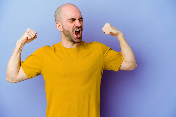 Young caucasian bald man isolated on purple background raising fist after a victory, winner concept. - Foto, afbeelding