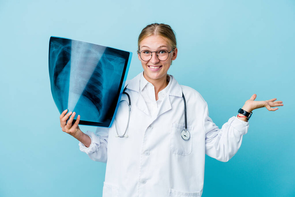 Young russian doctor woman holding a bone scan on blue celebrating a victory or success, he is surprised and shocked. - Photo, Image