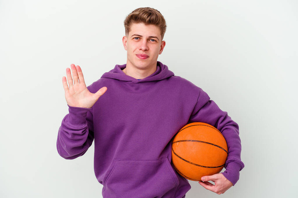 Junger kaukasischer Mann spielt Basketball isoliert Hintergrund lächelnd fröhlich zeigt Nummer fünf mit den Fingern. - Foto, Bild