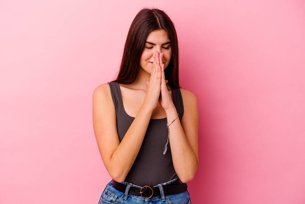 Joven mujer caucásica aislada sobre fondo rosa cogida de la mano en orar cerca de la boca, se siente segura. - Foto, Imagen