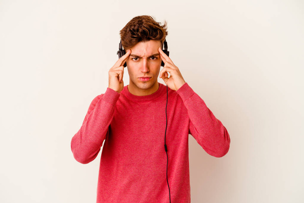 Young caucasian man listening to music isolated on white background focused on a task, keeping forefingers pointing head. - Φωτογραφία, εικόνα