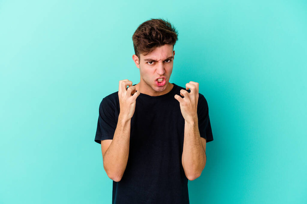 Young caucasian man isolated on blue background upset screaming with tense hands. - Foto, afbeelding