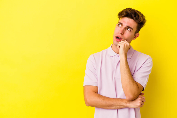 Young caucasian man isolated on yellow background relaxed thinking about something looking at a copy space. - Photo, Image