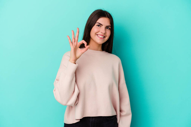 Young caucasian woman isolated on blue background cheerful and confident showing ok gesture. - Φωτογραφία, εικόνα