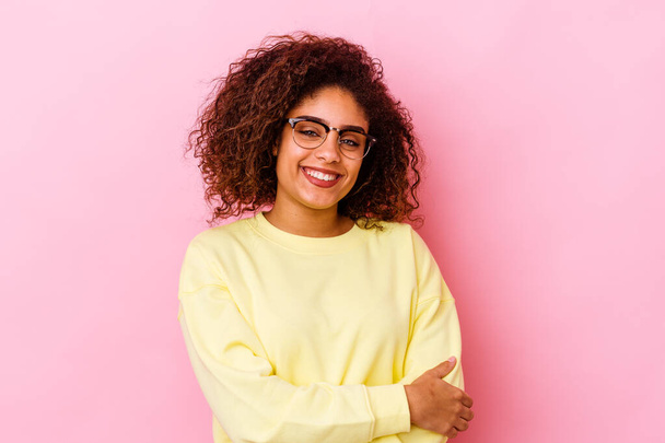 Young african american woman isolated on pink background who feels confident, crossing arms with determination. - Photo, Image