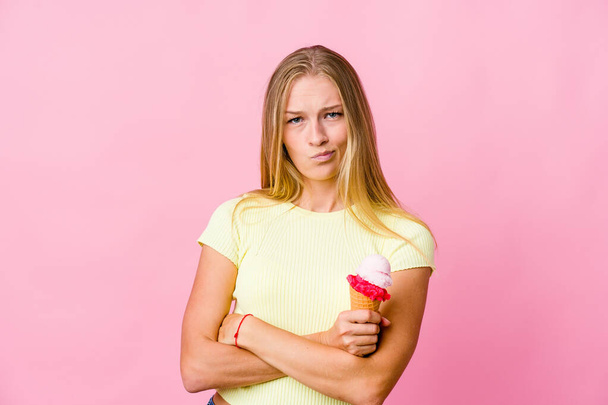 Young russian woman eating an ice cream isolated frowning face in displeasure, keeps arms folded. - Photo, Image
