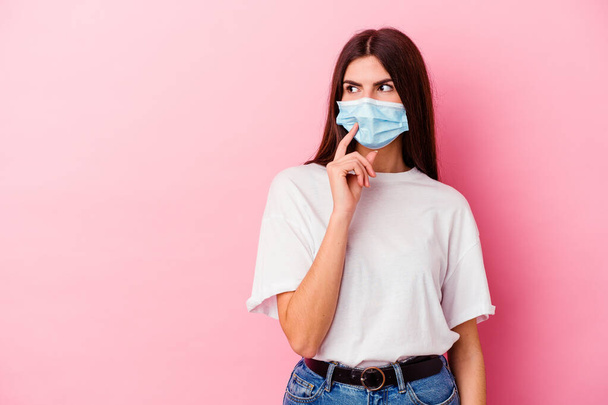 Young caucasian woman wearing a mask for virus isolated on pink background looking sideways with doubtful and skeptical expression. - Foto, immagini