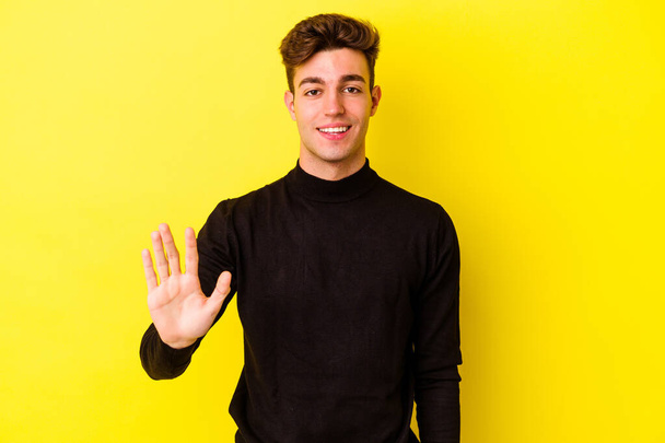Young caucasian man isolated on yellow background smiling cheerful showing number five with fingers. - Photo, Image