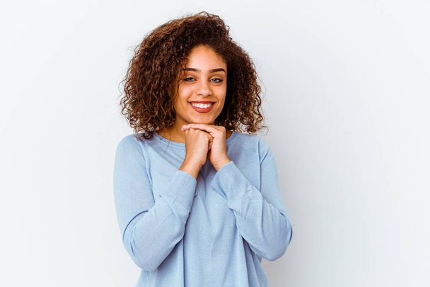 jovem afro-americana mulher isolada no fundo branco mantém as mãos sob queixo, está olhando alegremente de lado. - Foto, Imagem