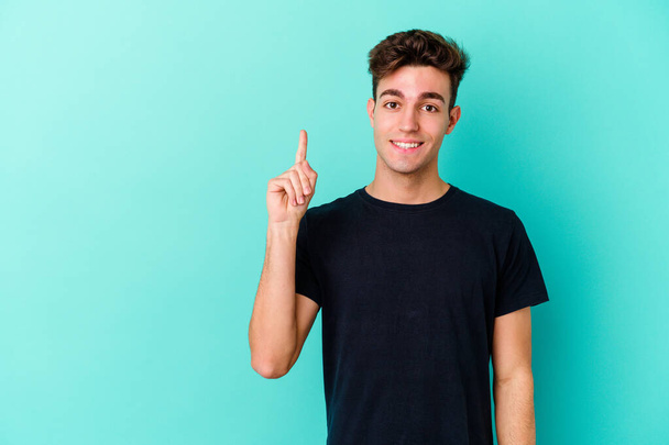 Giovane uomo caucasico isolato su sfondo blu mostrando il numero uno con il dito. - Foto, immagini