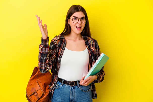Young student woman isolated on yellow background receiving a pleasant surprise, excited and raising hands. - Photo, Image