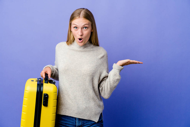 Joven mujer rusa sosteniendo maleta para viajar impresionado sosteniendo espacio de copia en la palma. - Foto, imagen